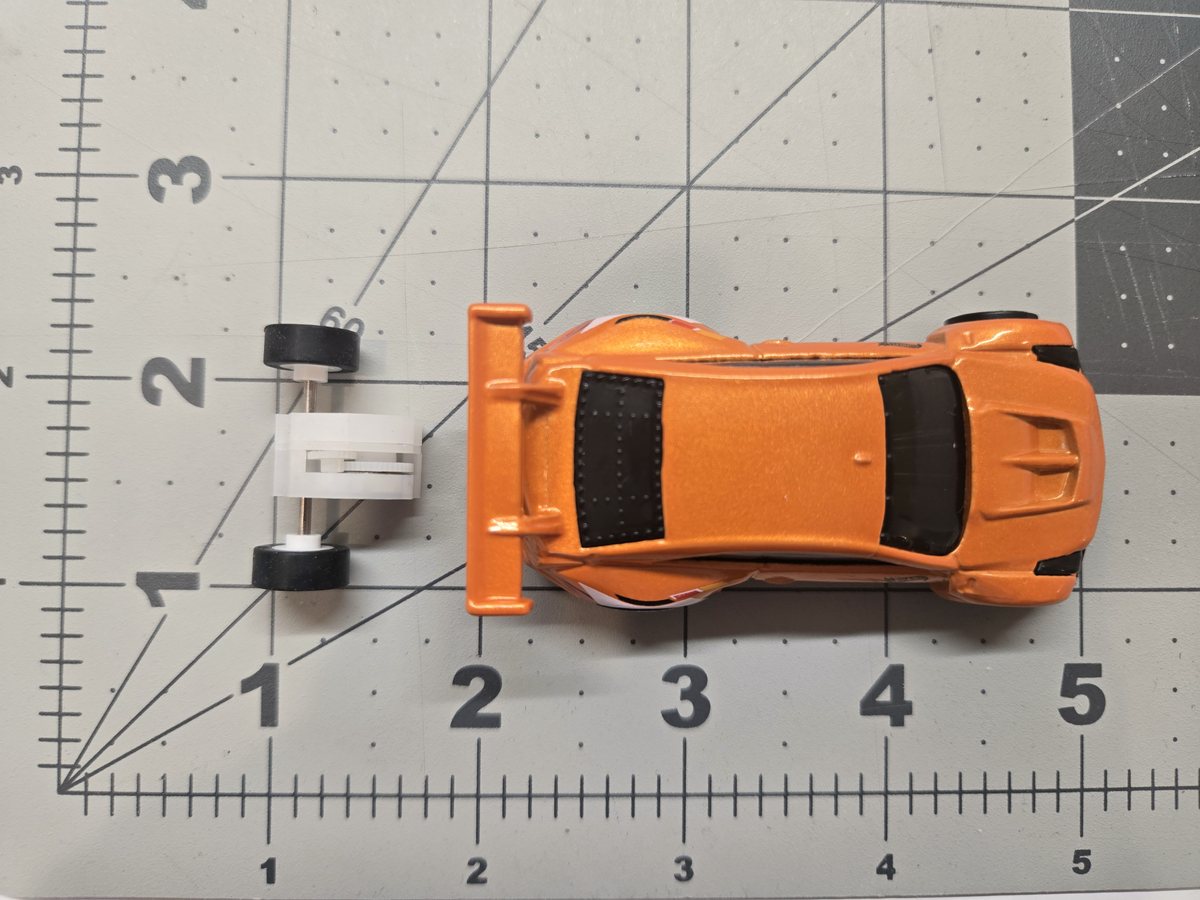 An Ant pull-back motor and its front axle seen from above on a measuring mat, beside a 1/64 scale diecast car of almost the same width