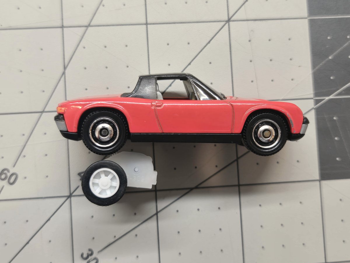 An Ant pull-back motor sitting beneath a slim, low-bodied 1/64 diecast sports car