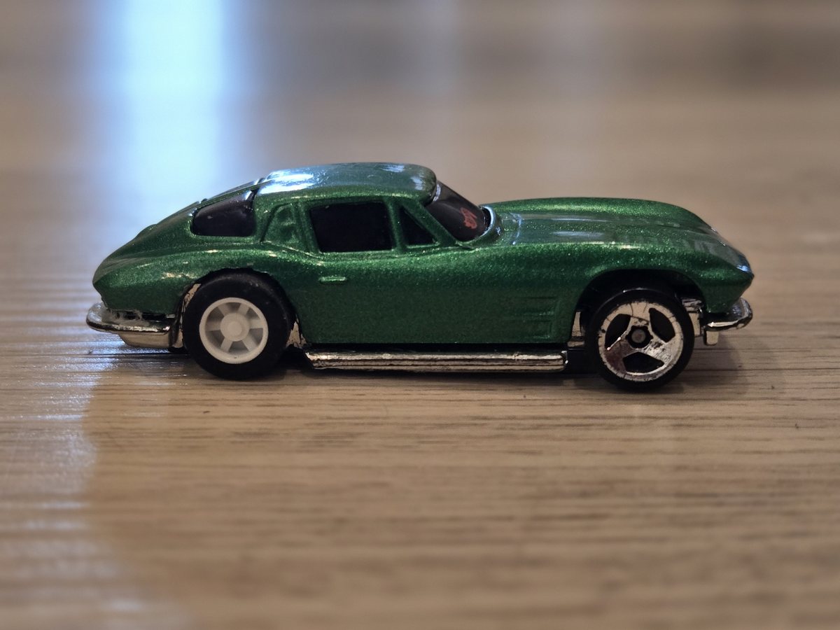 A green 1/64 diecast sports car in profile with a Stout pull-back motor built inside it